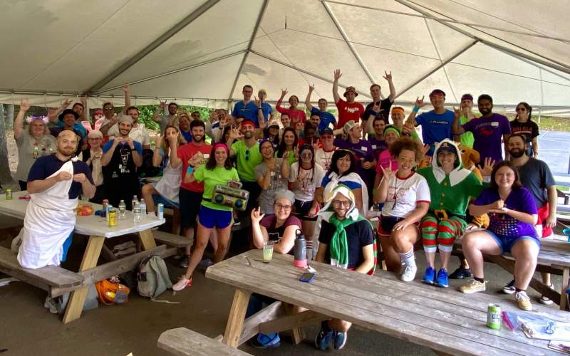 A large group of costumed employees are gathered under a tent, showing various ASL hand signs (mostly saying, I love you!)