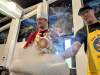 Two employees, both wearing aprons and one with a chef's hat, tend to a cauldron of dry ice.